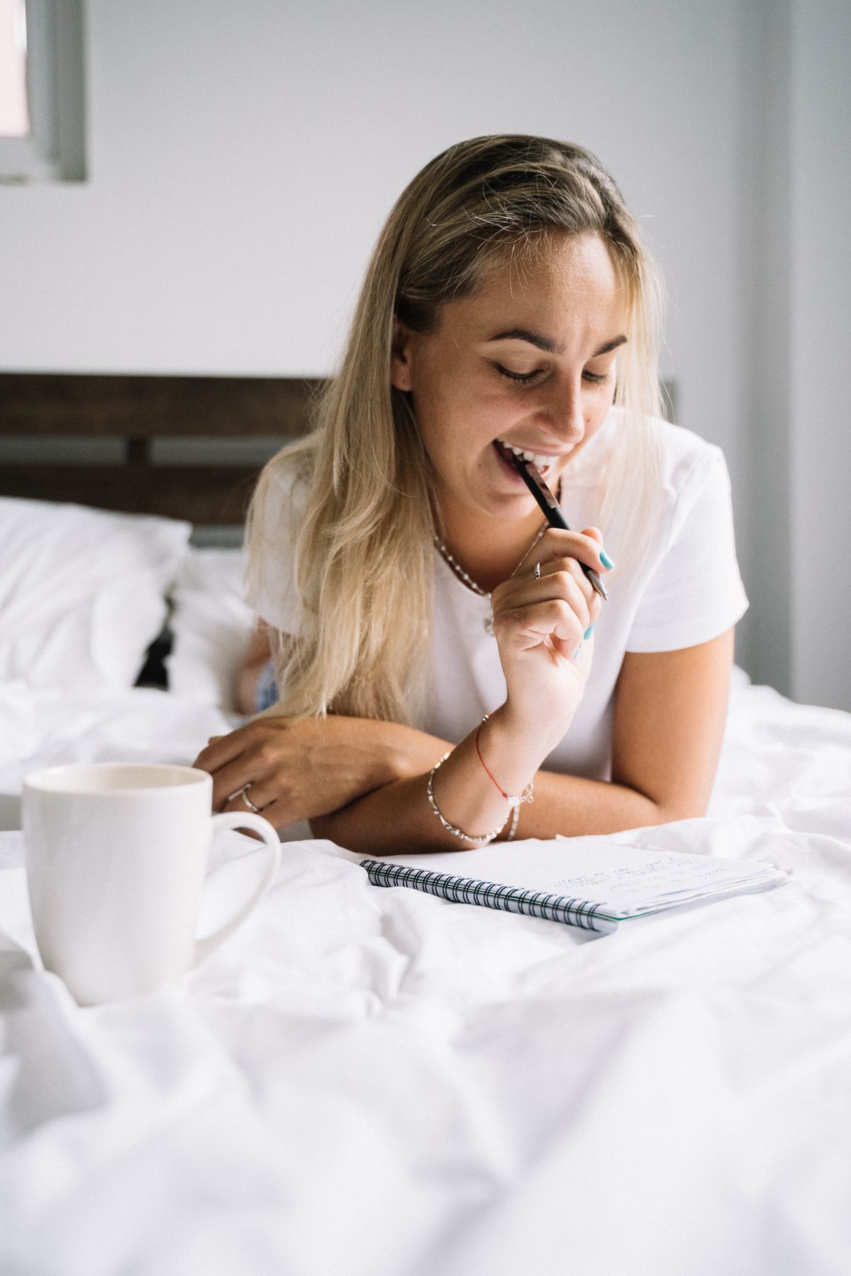 A woman journaling on a bed with a mug beside her