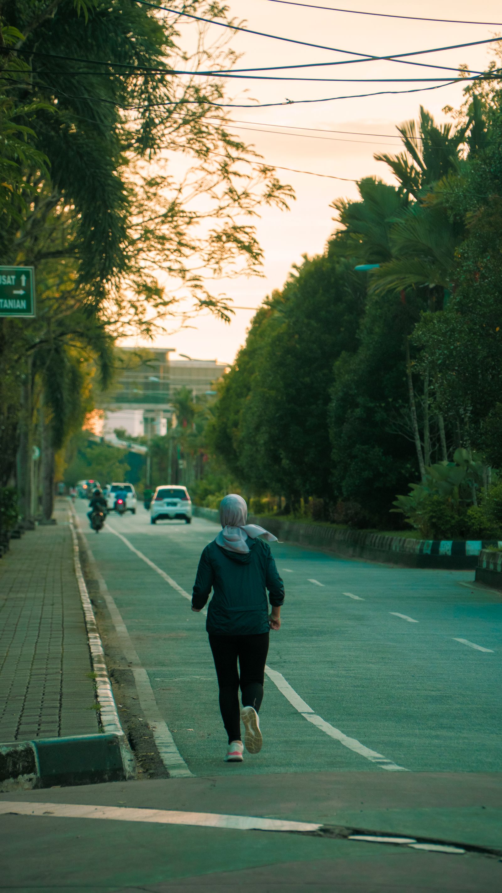 A woman jogging down a tree-lined street at sunrise
